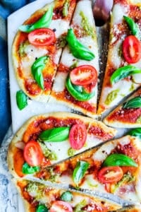 Two pizzas on a cutting board on a white counter top.