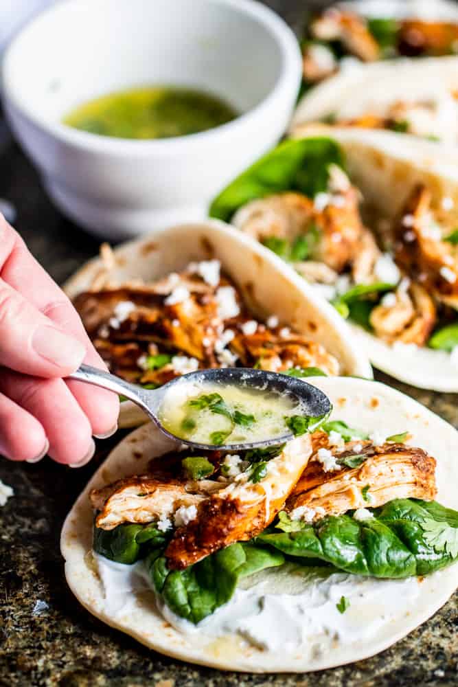 Hand drizzling cilantro lime butter over chicken tacos.
