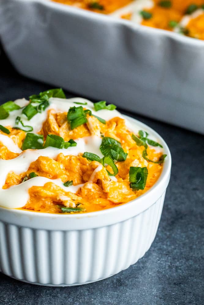 Shot of buffalo dip in a white bowl with ranch and green peppers on top.