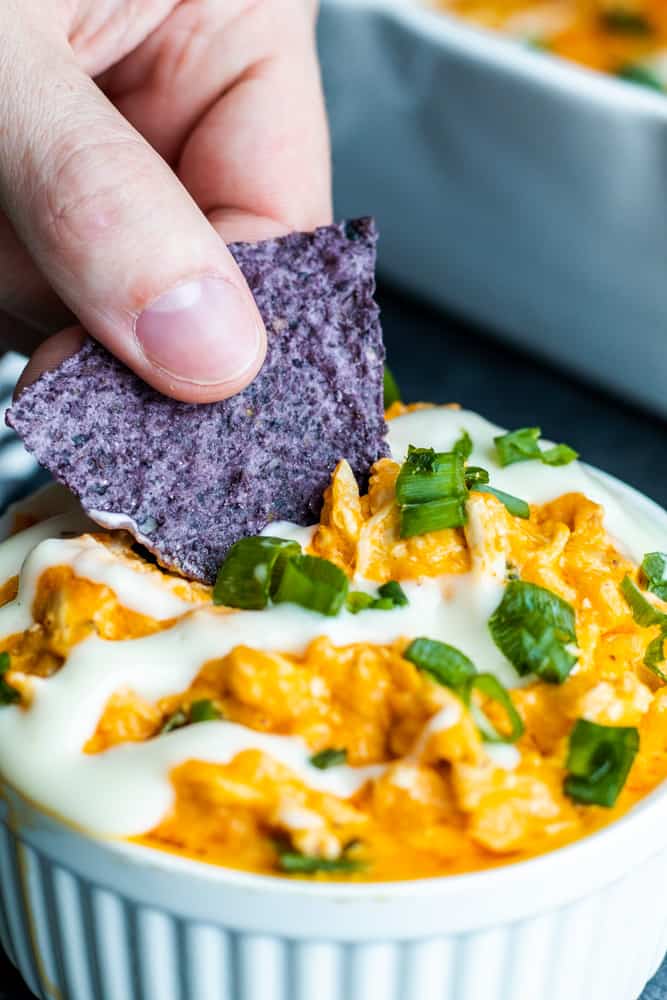 Hand dipping blue tortilla chip into white bowl of dip. 