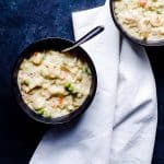 Overhead shot of two black bowls of chicken and dumplings on a blue counter.