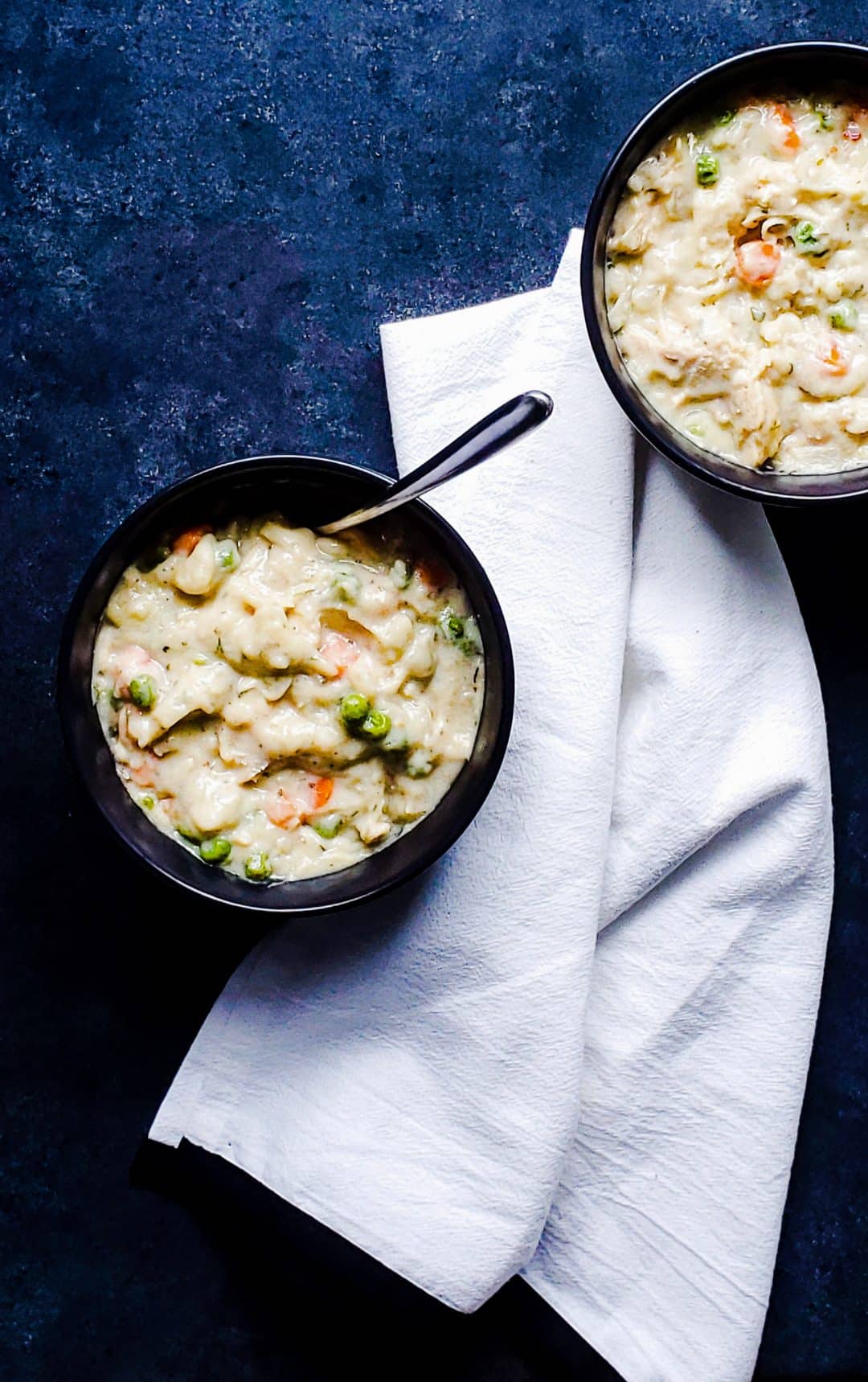 Overhead shot of two black bowls of chicken and dumplings on a blue counter.