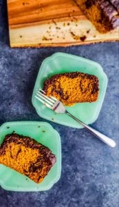 Two pieces of pumpkin spice loaf cake on teal plates on a gray count top.