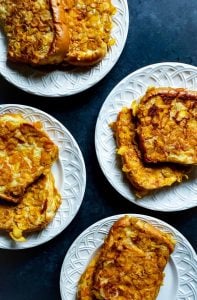 Four white plates on a blue counter with french toast on them.