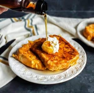 French toast on a white plate with syrup being poured on top.