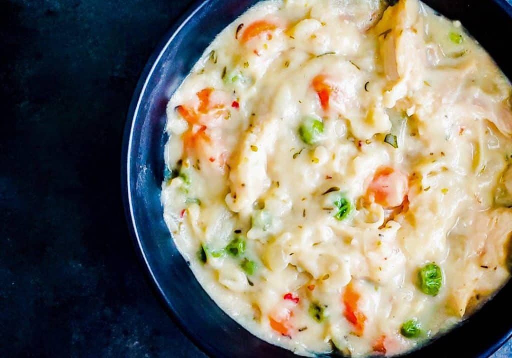 A close up shot of crockpot chicken and dumplings with biscuits in a black bowl. The shot is from above and you can see all the detail of the peas and carrots in the bowl.