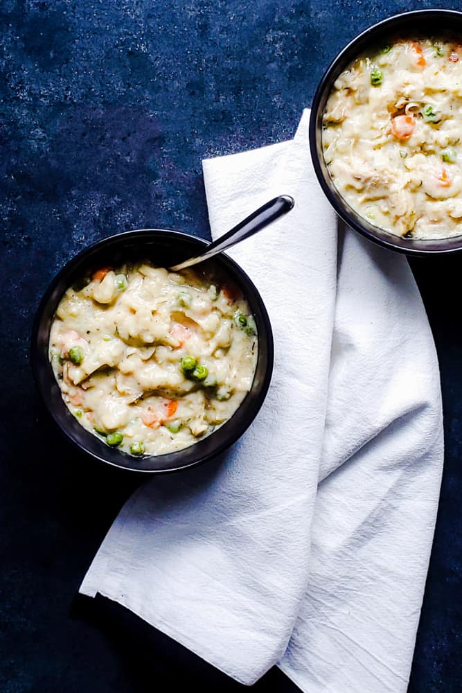 Overhead shot of two bowls of chicken and dumplings on a blue counter.