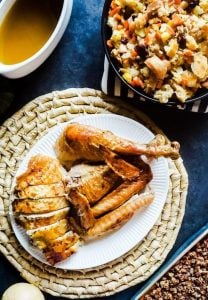 Herb butter roasted turkey on a white serving platter on a blue counter with assorted sides around it.