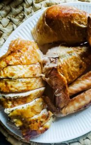 The image is a close up shot of the the herb butter roasted turkey sliced up on a white plate. The white plate is a on tan basket weave place mat. 