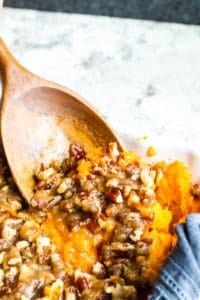 Wooden spoon scooping out sweet potato casserole in a white dish.