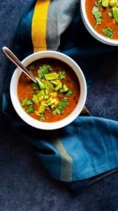 Black Bean soup in a white bowl with silver spoon in it on a blue counter.