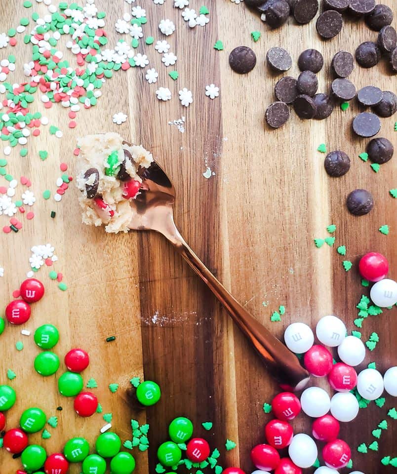 Overhead shot of cookie dough on a gold spoon with candy, sprinkles and chocolate surrounding it.