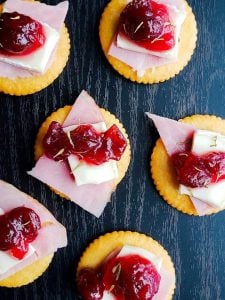 Image for Ritz Bites with Ham, Brie and Cranberries. The image is shot from above and shows a close up of multiple bites on a black surface.