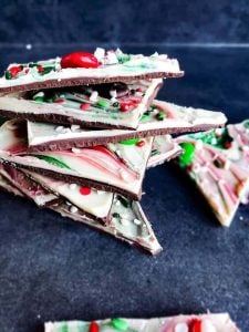 Image for Christmas chocolate bark recipe, The image is taken at a angle and shows the bark stacked on top of each other on a blue counter.