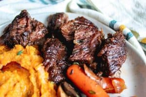 Image for crockpot beef short ribs recipe. Close up shot of the beef on a white plate with a white napkin in the background. 