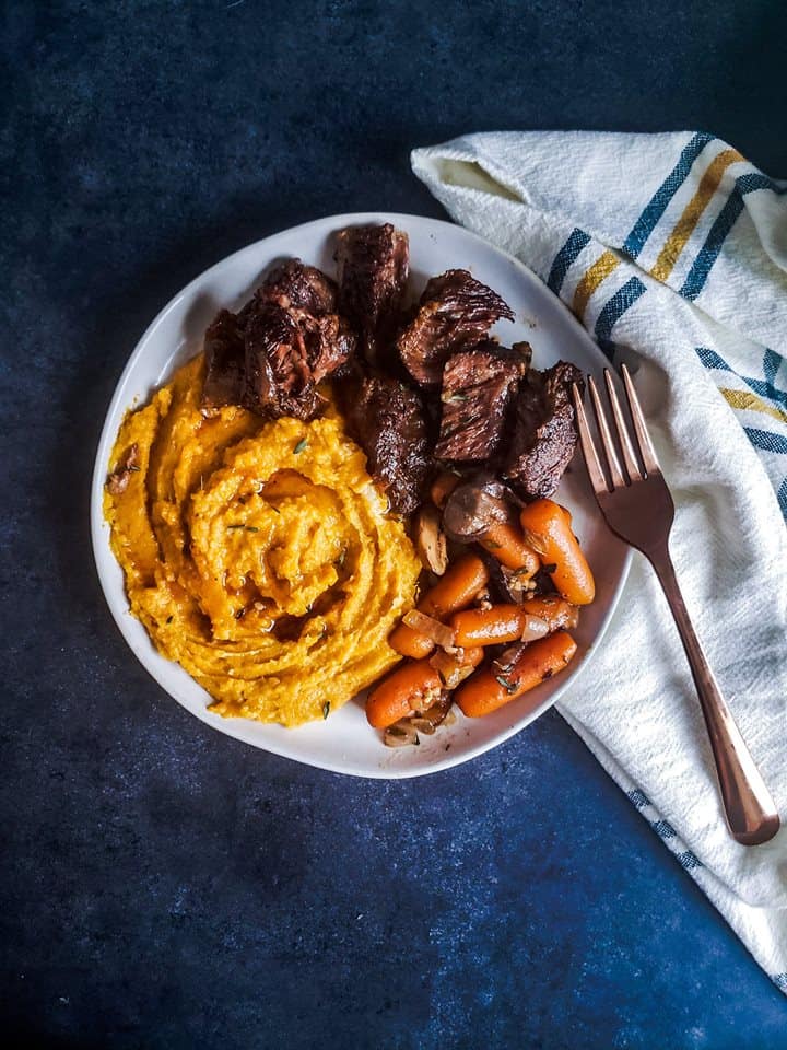 White plate with short ribs and sides on it.