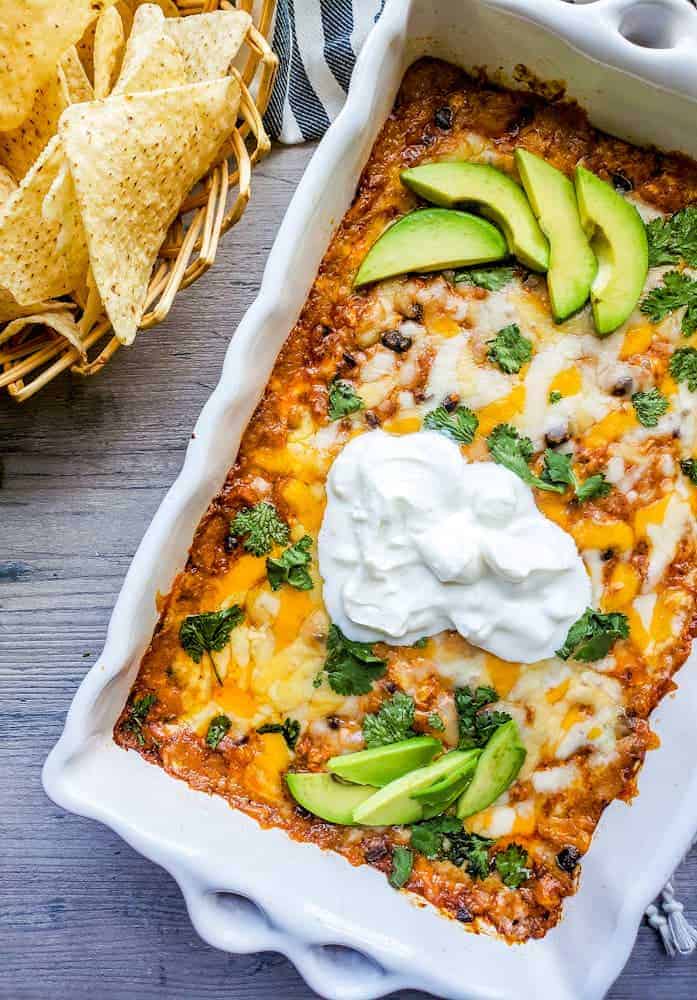 Baked chicken dip in a white baking dish with chips on the side.