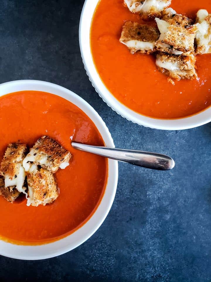 Overhead shot of two white bowls of soup with one having a spoon in it.