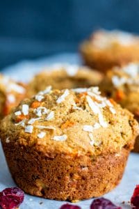 Close up shot on one single muffin. The muffin is centered and there are muffins blurred out in the background. The muffin is sitting on a white piece of parchment paper and the background is dark blue.