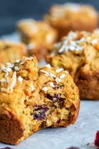 Close up shot strait on of one muffin. The muffin has a bite out of it and shows the inside. There are multiple in the background blurred out.