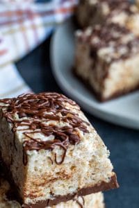 Close up shot of rice krispie treat with a white plate of more blurred out in the background. There is also a plaid towel blurred out in the background.