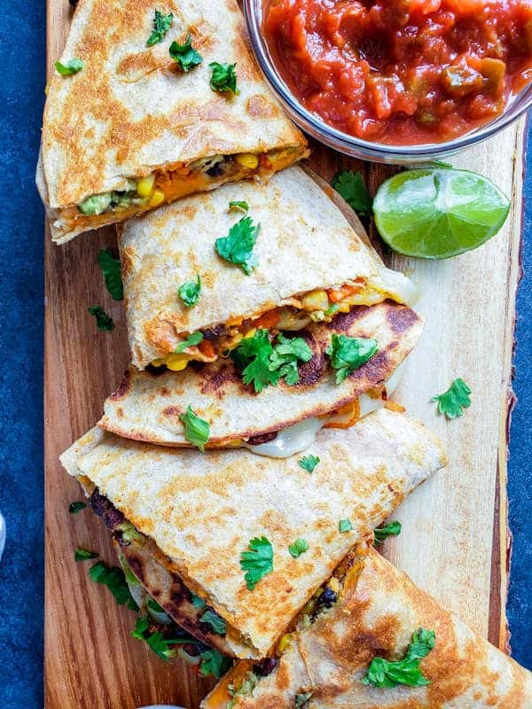 Overhead shot of sliced quesadilla on wooden cutting board.