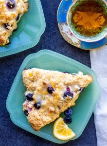 Overhead shot of two blueberry scones on teal plates with a cup of tea. 