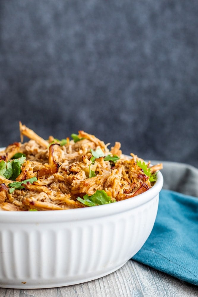 Cooked Crockpot Pork Carnitas in a white bowl on a white wood counter.