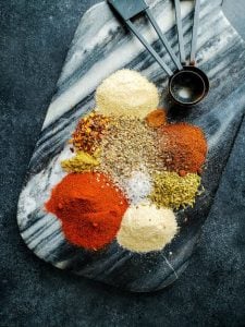 Image of all Mexican Spices on a blue and white marble cutting board.