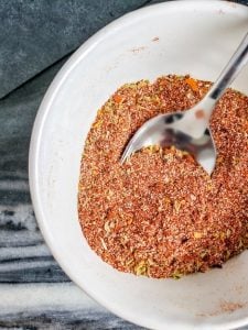 Homemade taco seasoning in a white bowl with a silver spoon in it.