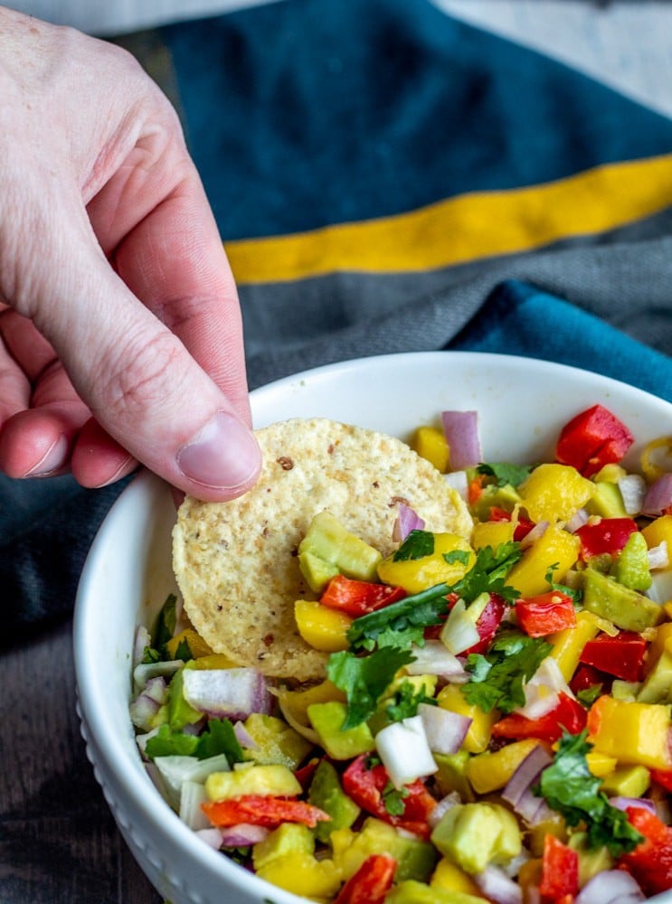 Hand dipping chip  into bowl of salsa.