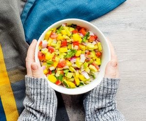 Salsa in a white bowl with two hands holding it.