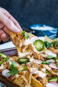 Hand picking up a chip covered in cheese, pork and jalapeno. 