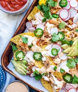 Pork Carnitas nachos on a baking tray with salsa and sauce bowls around it.