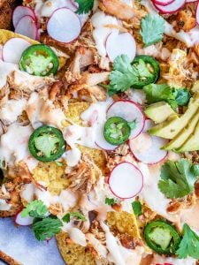 Overhead shot of nachos on a pan topped with avocado, pork and cheese.