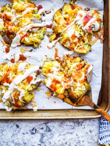 Buffalo smashed potatoes on a baking sheet with gold spatula picking up one.