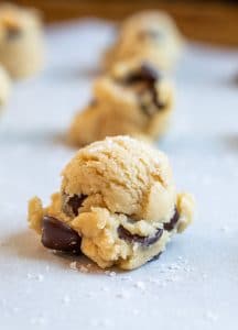 Close up of raw cookie dough on a cookie sheet with more blurred in background. 