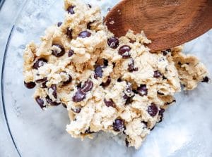 Raw cookie dough in a glass bowl with wooden spoon.