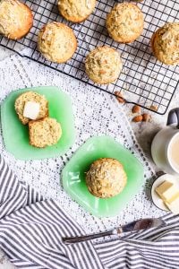 This Almond Poppy Seed Muffins recipe is easy, fast and perfect for breakfast, brunch, snacks of a dessert. These muffins are also great for toddlers and the rest of your family. #vegetarian #muffins #breakfast #snacks #almonds Overhead shot of two almond poppy seed muffins on green plates with some others on a baking rack.