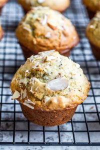 This Almond Poppy Seed Muffins recipe is easy, fast and perfect for breakfast, brunch, snacks of a dessert. These muffins are also great for toddlers and the rest of your family. #vegetarian #muffins #breakfast #snacks #almonds #poppyseed Close up of single muffin on a black wire cooling rack with others blurred in background.