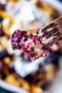 Gold fork holding a piece of french toast with a blackberry. 