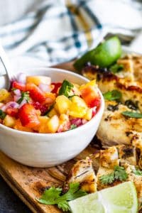 Image of Strawberry Pineapple salsa in a white bowl with chicken on the right.