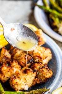 Silver spoon pouring lemon butter sauce over chicken on a blue plate.