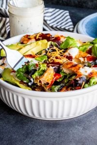 Silver fork dipping into white bowl filled with BBQ Chicken salad.