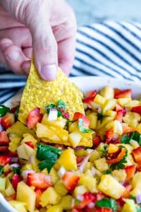 Hand reaching into strawberry pineapple salsa with a tortilla chip.