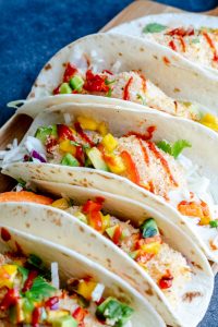 Shot of fish tacos on a tray on a blue counter top. 