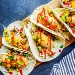 These Baked Coconut Crusted Healthy Fish Tacos with Mango Avocado Salsa is the best, easy recipe for a quick under 30 minute family weeknight dinner! The cod is baked in the oven until crispy, then paired with cilantro lime cabbage slaw for the perfect finish. {VIDEO} #fish #food #healthy #bakedfish #tacos