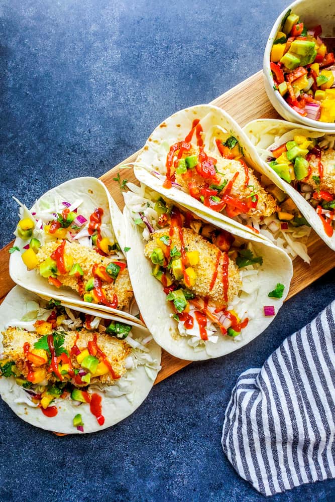 These Baked Coconut Crusted Healthy Fish Tacos with Mango Avocado Salsa is the best, easy recipe for a quick under 30 minute family weeknight dinner! The cod is baked in the oven until crispy, then paired with cilantro lime cabbage slaw for the perfect finish. {VIDEO} #fish #food #healthy #bakedfish #tacos