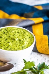 Chimichurri sauce in a white bowl with a blue cloth in the background. 