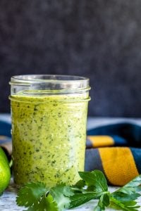 Chimichurri sauce in a glass mason jar with herbs next to it.